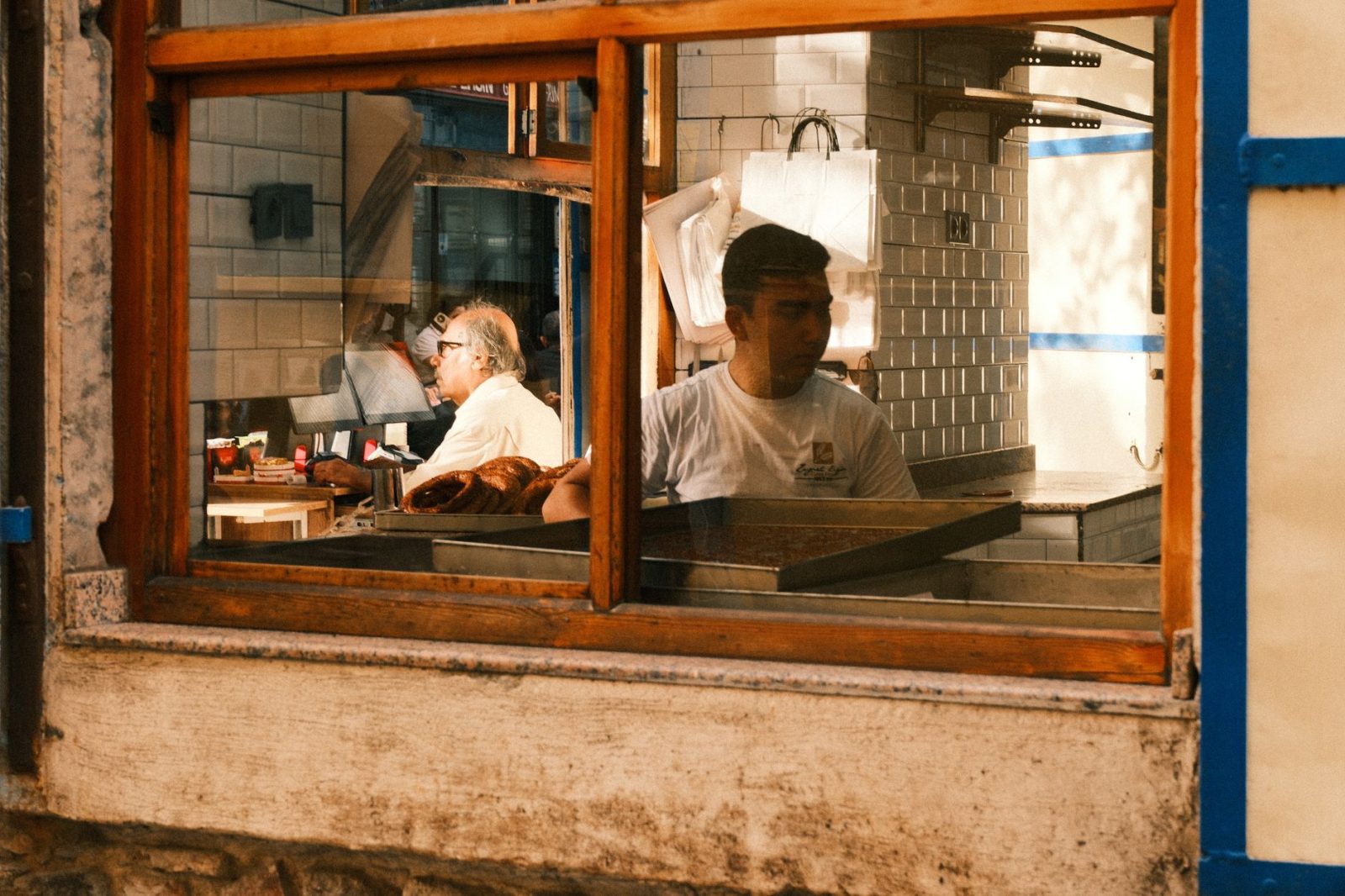 Blick durch das Fenster einer Bäckerei auf zwei Mitarbeiter bei der Arbeit