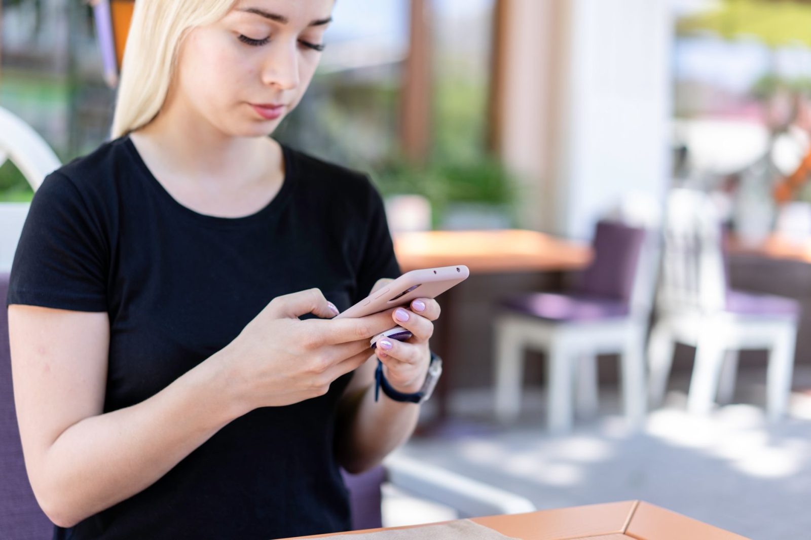 Eine junge Frau tippt an einem Außentisch auf ihrem Handy
