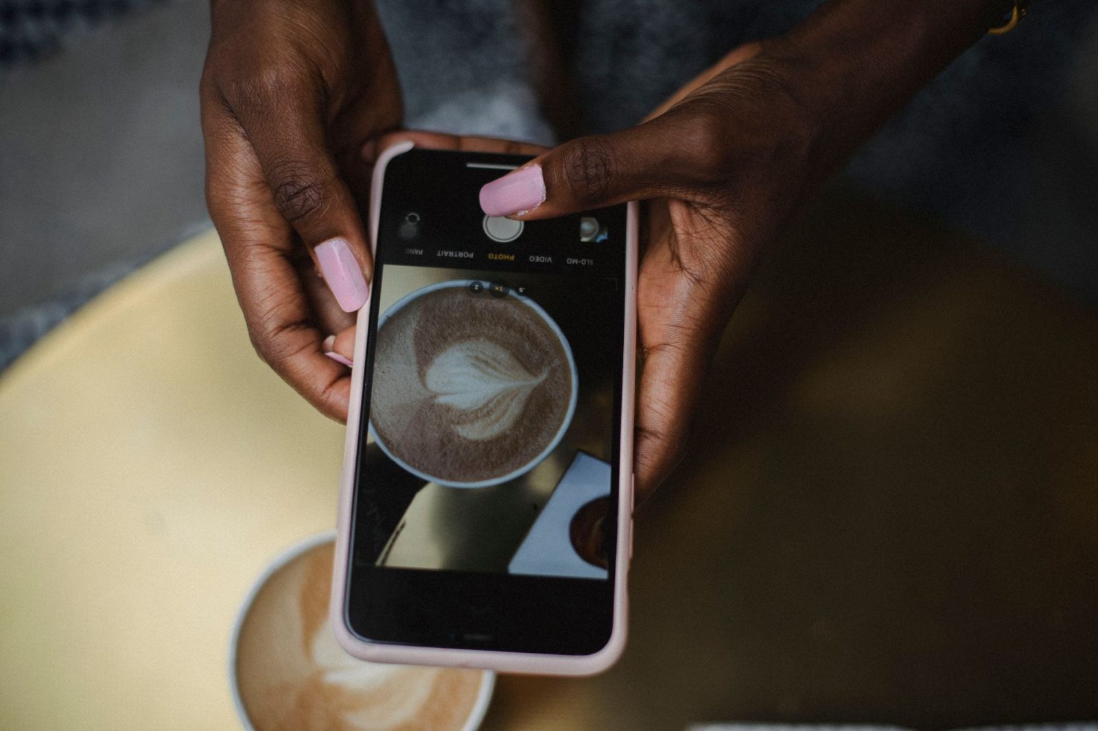 Jemand fotografiert einen Milchkaffee mit dem Handy